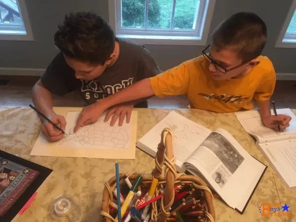 2 boys using history book to help them do map work