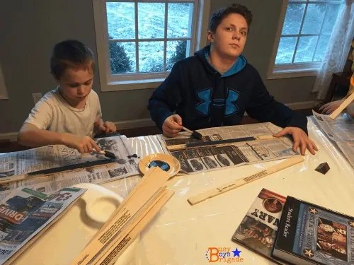boys sitting at a table painting paint sticks to make history timelines