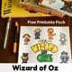 Free printable Wizard of Oz Learning Fun pack on dark wood desk with gold pen & orange mechanical pencil and Wizard of Oz books & DVD case