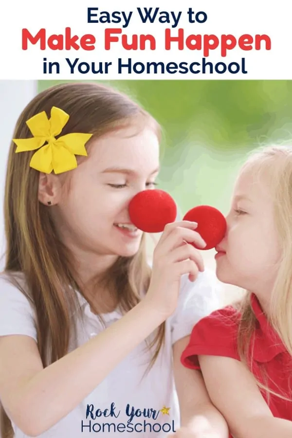 Brunette sister with yellow flower in her hair & wearing a red nose is smiling at blonde little sister with red nose