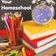 Purple clock on stack of books with colored pencils & scissors on wood surface with black chalkboard background