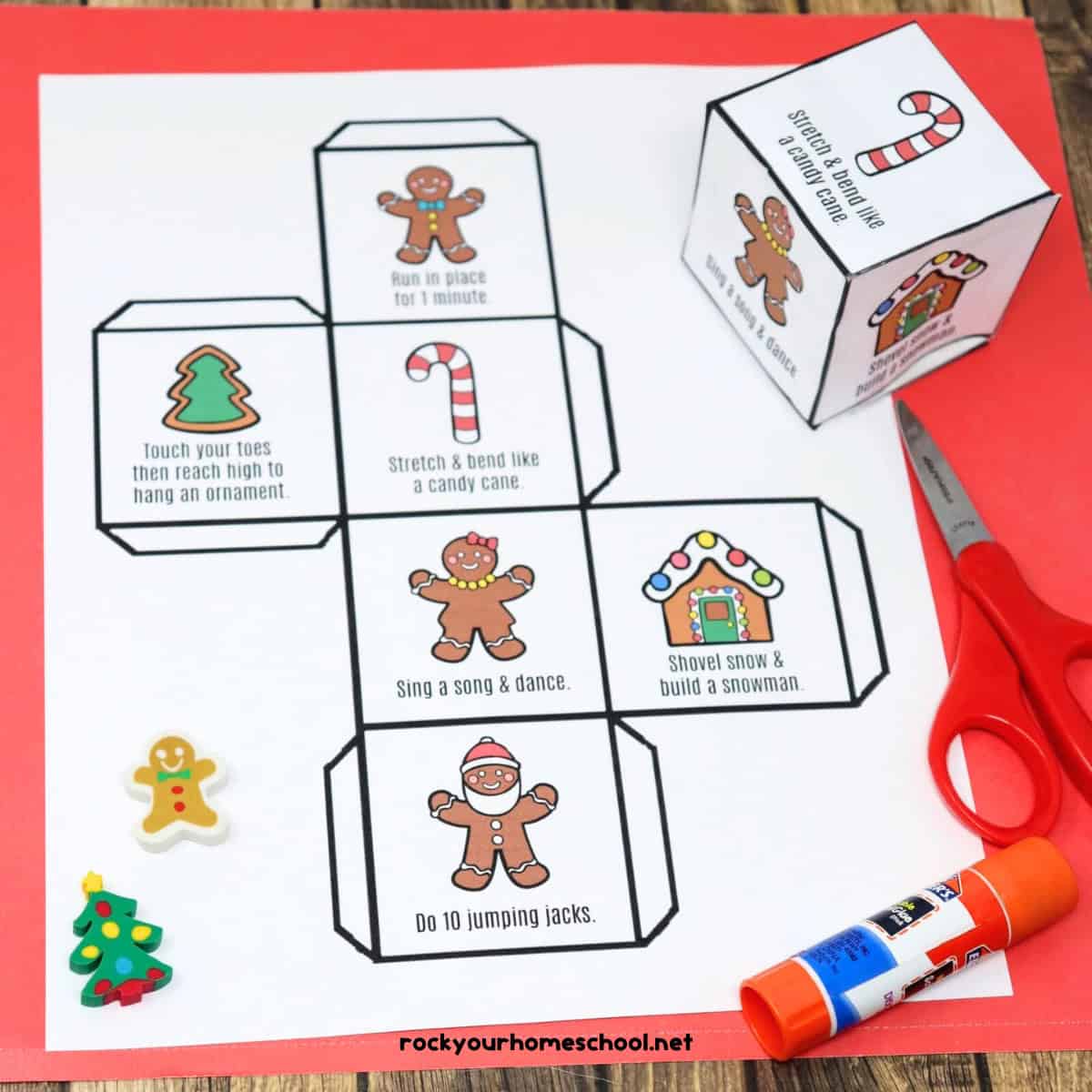 Gingerbread man activity cube printable page and cube with scissors and glue stick on red paper with wood background.