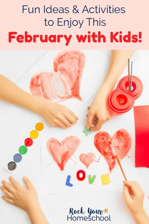 The hands of two kids using watercolor paints to make hearts & red paper & magnet letters spelling love on white background