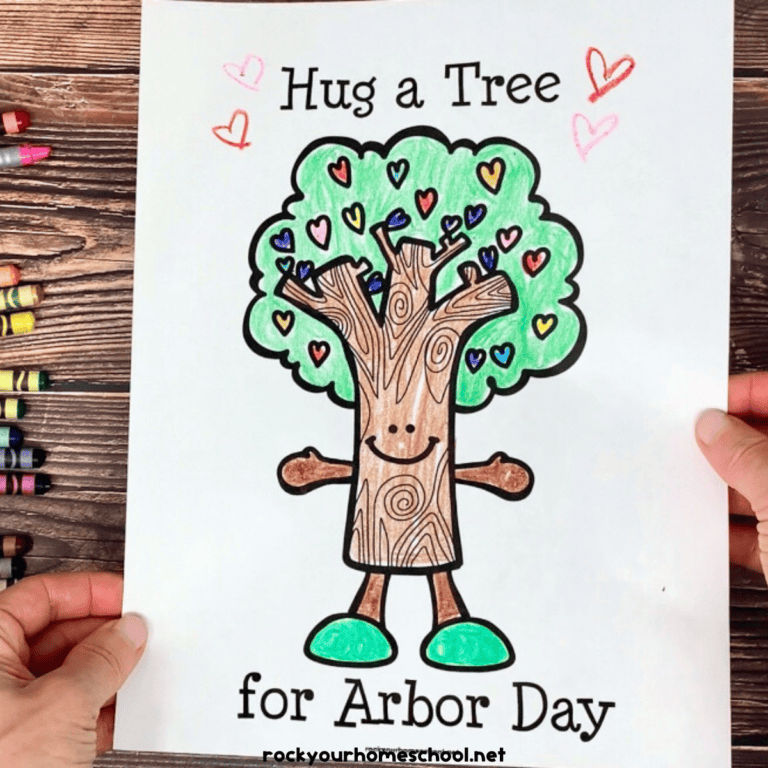 Woman holding free printable Arbor Day coloring page with crayons in background.