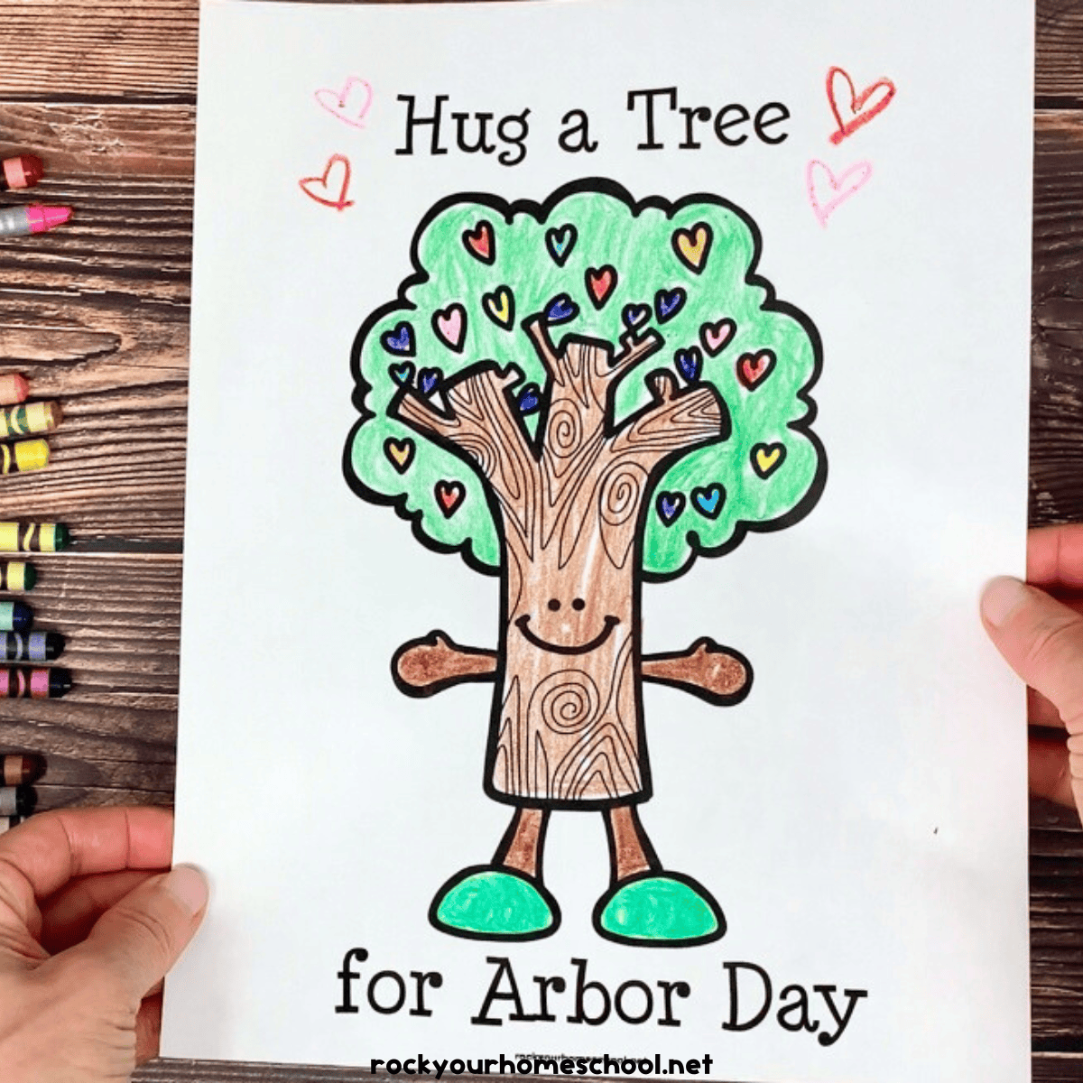 Woman holding free printable example of Arbor Day coloring page with crayons in background.