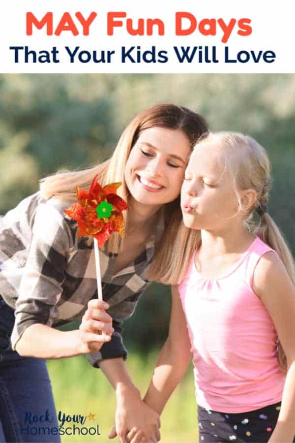 Mom & daughter smiling as daughter blows on pinwheel with trees & grass in background