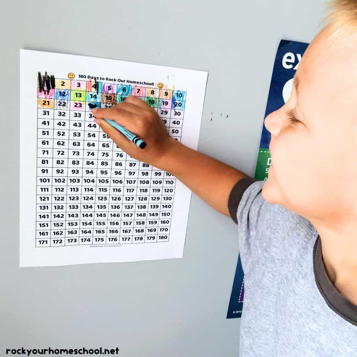 Young boy using crayon to mark off day on track your homeschool year chart for 180 days.