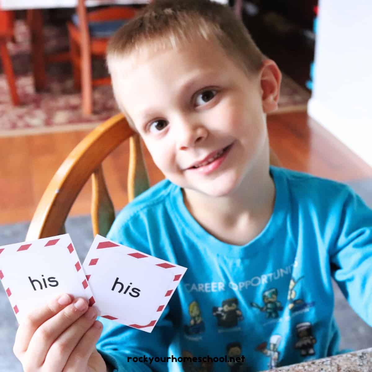 Young boy smiling as he holds two sight words memory game cards.