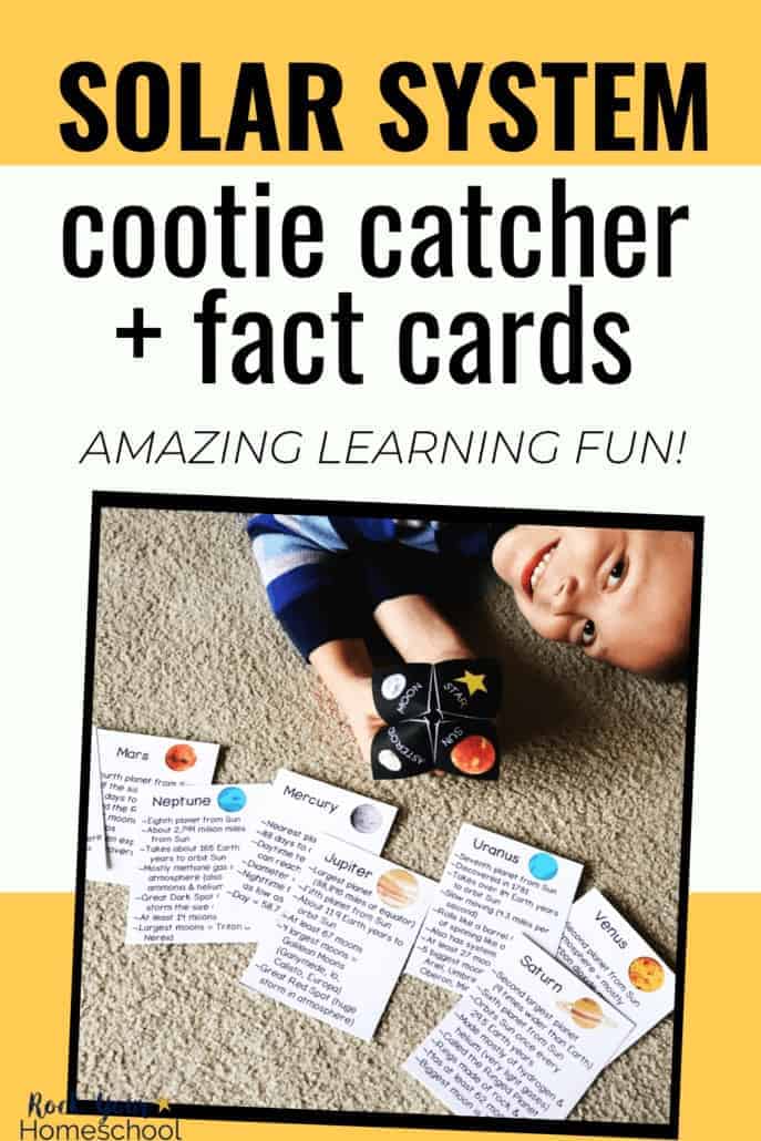 Boy smiling and holding solar system cootie catcher with planet fact cards in front of him on the carpet to feature the science learning fun to be had with this activity pack