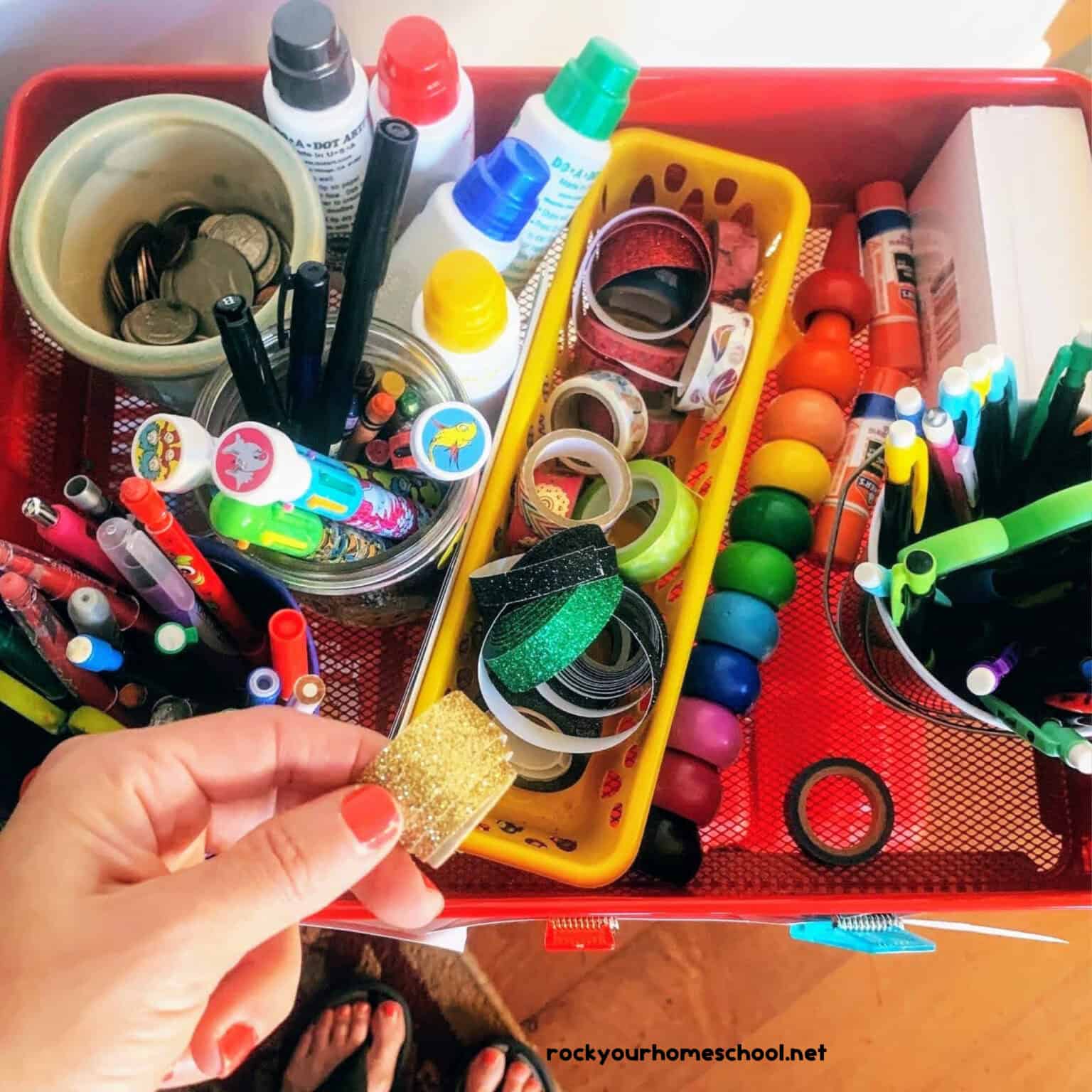 Mom holding washi tape with other practical homeschool supplies like scissors, erasable pens, pencils, and more in the background.