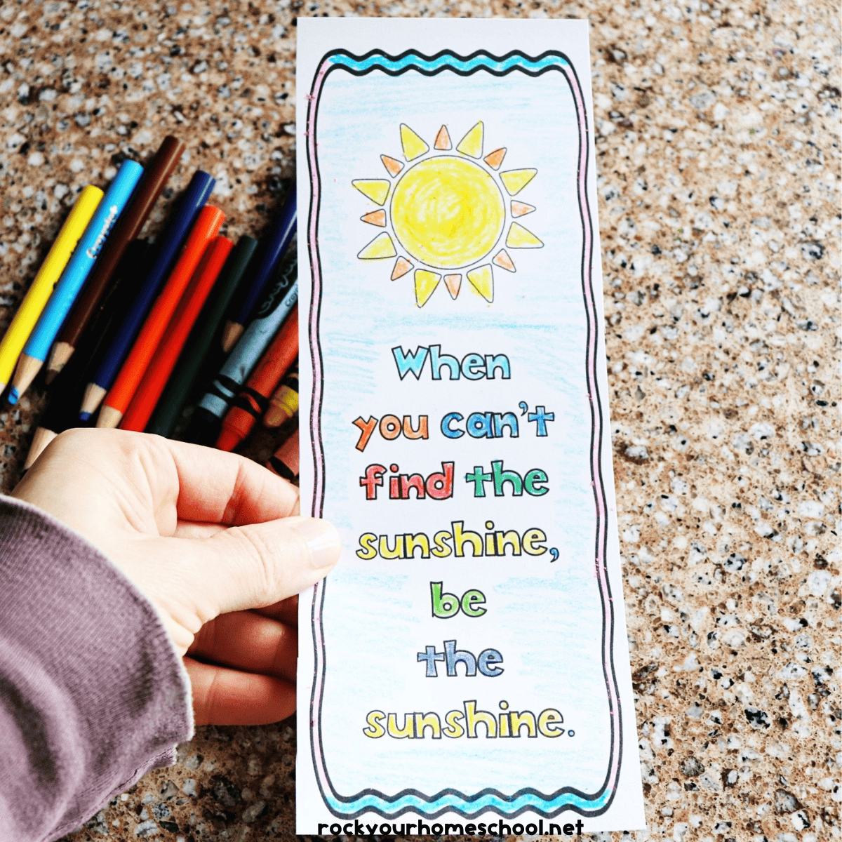 Woman holding growth mindset coloring bookmark with color pencils in background.