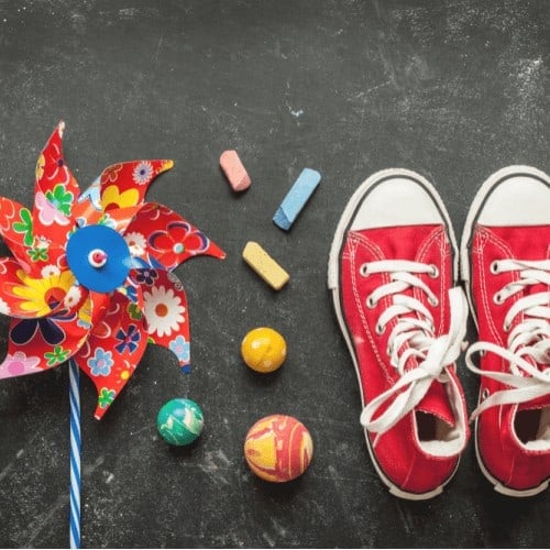 red floral pin wheel with colored chalk, bouncy balls, and red Converse shoes on black chalkboard to feature how you can make life and learning fun with Rock Your Homeschool