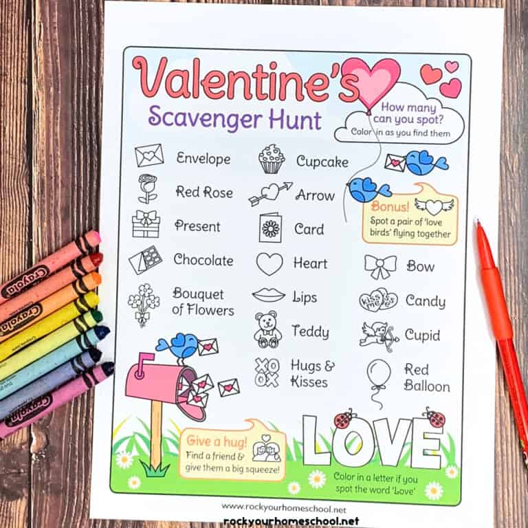 Free Valentine's Day scavenger hunt with red pencils and rainbow of crayons on wood surface.