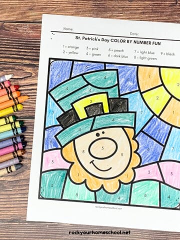 St. Patrick's Day color by number pages with a leprechaun and horseshoe and three-leaf clover with crayons on wood surface.