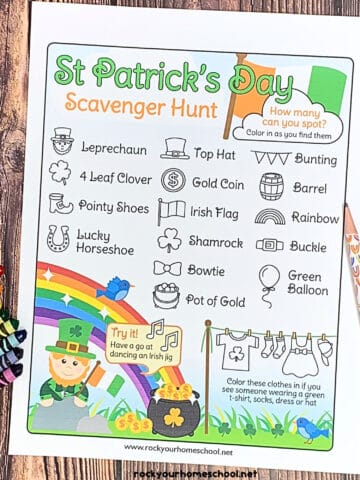 free printable St. Patrick's Day scavenger hunt with crayons and pencils with rainbows on wood surface.