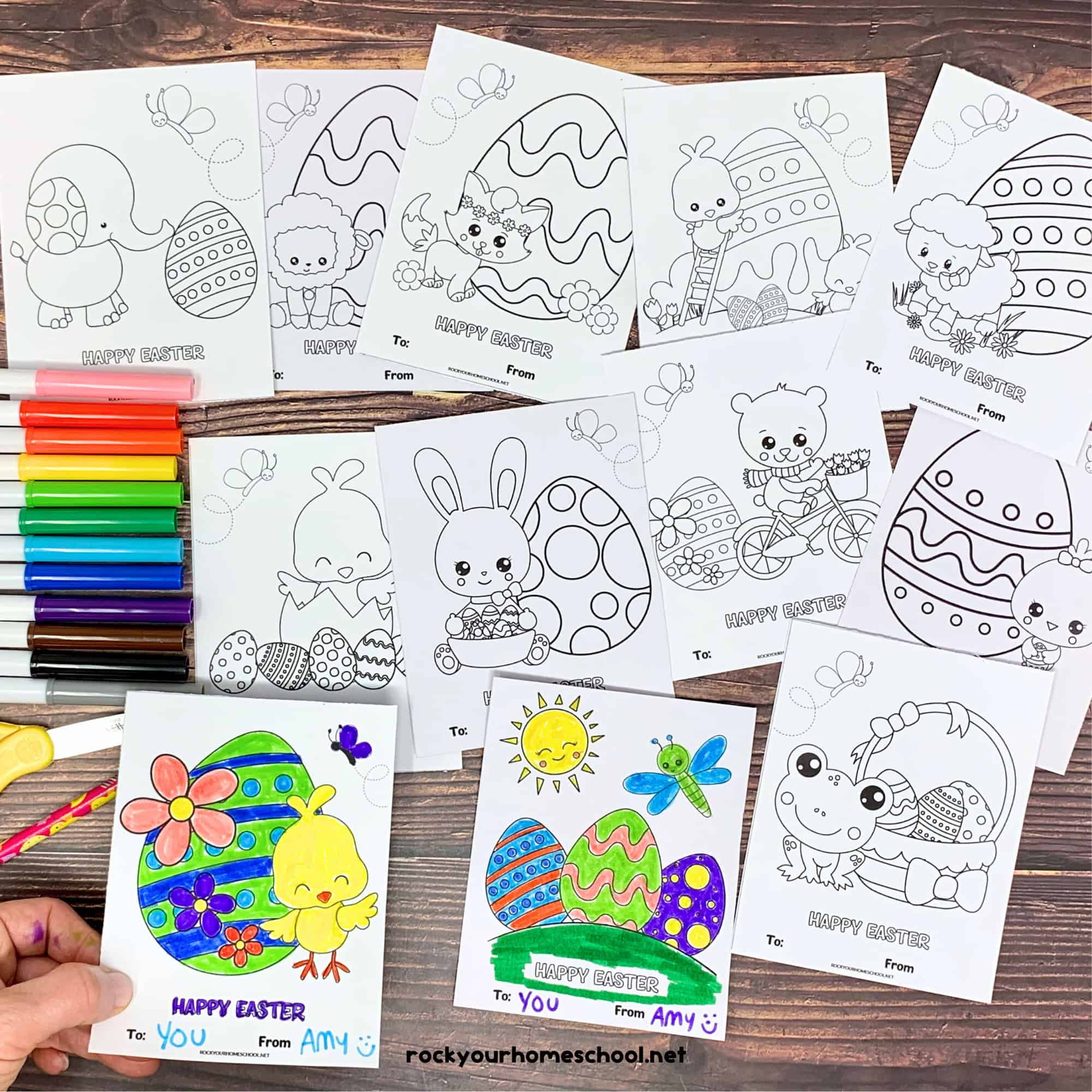 12 free printable Easter cards for kids with rainbow of markers, yellow scissors, and pink pencil on wood background.