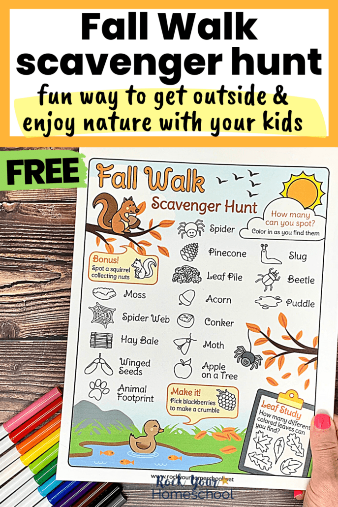 woman holding free printable fall walk scavenger hunt with rainbow of markers on wood background