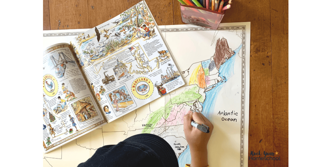 Young boy using marker to work on large foldable map of the United States with book opened to Maryland in background