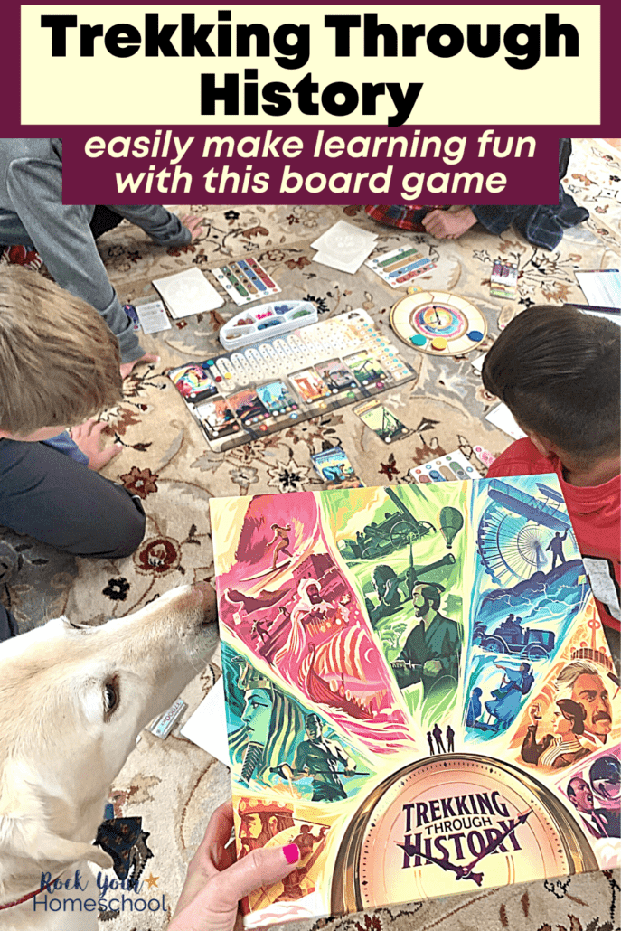 Woman holding Trekking Through History board game with dog interested in it and 4 boys in background relaxing as they play the game on a carpet