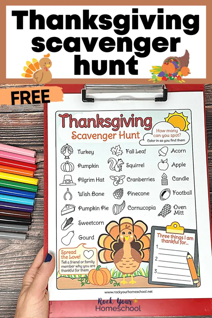 Woman holding red clipboard with free Thanksgiving scavenger hunt on wood background with rainbow of markers