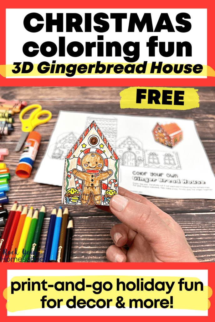 woman holding example of 3D Christmas craft featuring free printable gingerbread house coloring page with color pencils, markers, crayons, yellow scissors, and glue stick on wood background