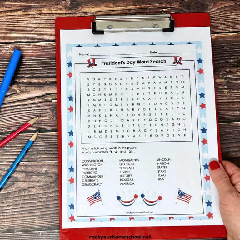 woman holding free printable President's Day word search on red clipboard with red and blue pencil and highlighter on wood background.