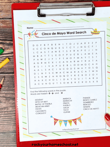 Woman holding red clipboard with Cinco de Mayo word search with red pencil and markers.