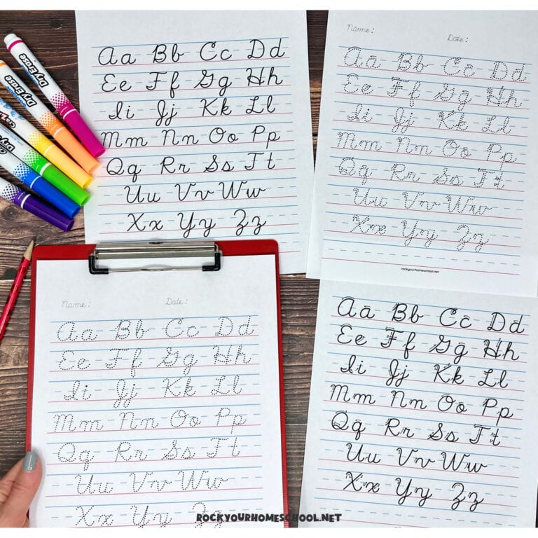 Woman holding red clipboard with free cursive alphabet chart printable with other practice pages and pencil and dry erase markers on wood background.