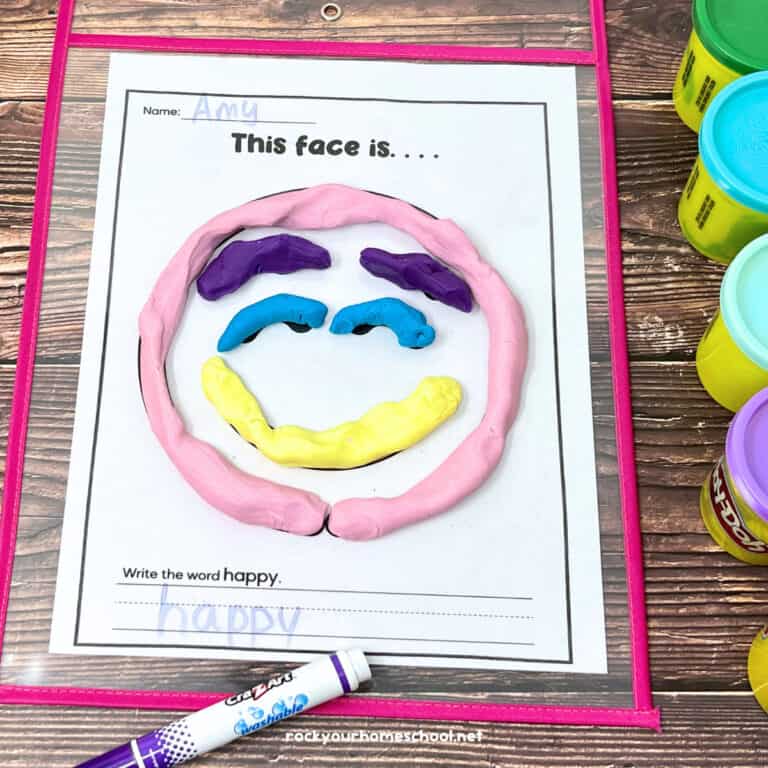 Emotion playdough mat featuring a smiling happy face in a dry erase sleeve pocket with marker and cans of playdough.