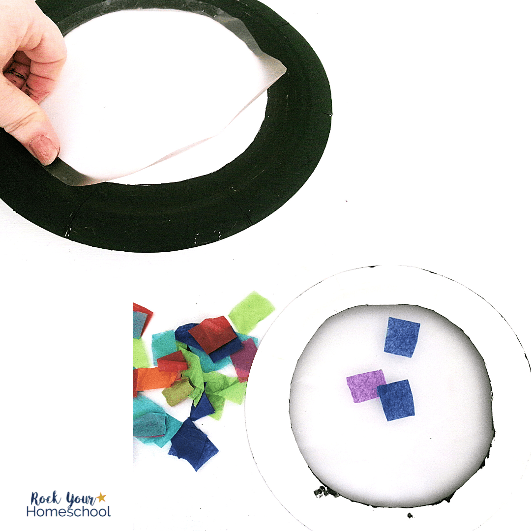 woman applying clear contact paper on black paper plate and tissue paper squares for hot air balloon suncatcher craft