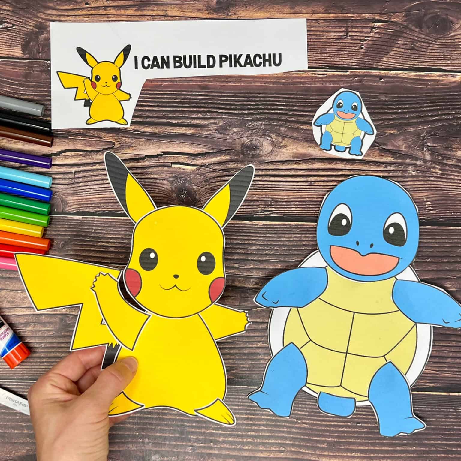 Woman holding Pickachu printable craft and Squirtle craft to feature this free printable set of Pokemon crafts.