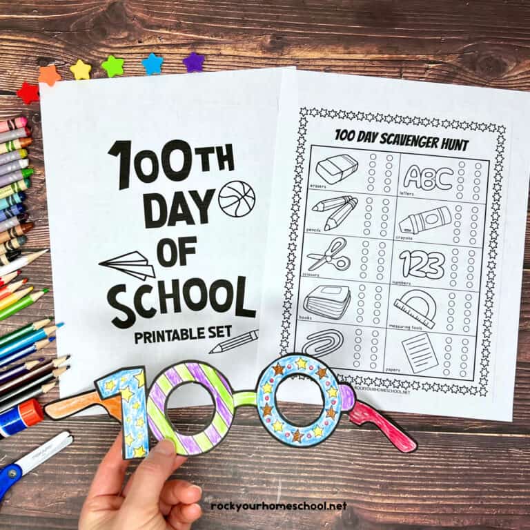 Woman holding paper glasses with 100 and examples of 100th day of school printables with crayons, color pencils, glue stick, and star mini-erasers.
