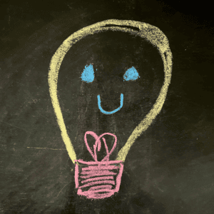 Black chalkboard with chalk lightbulb with smile.