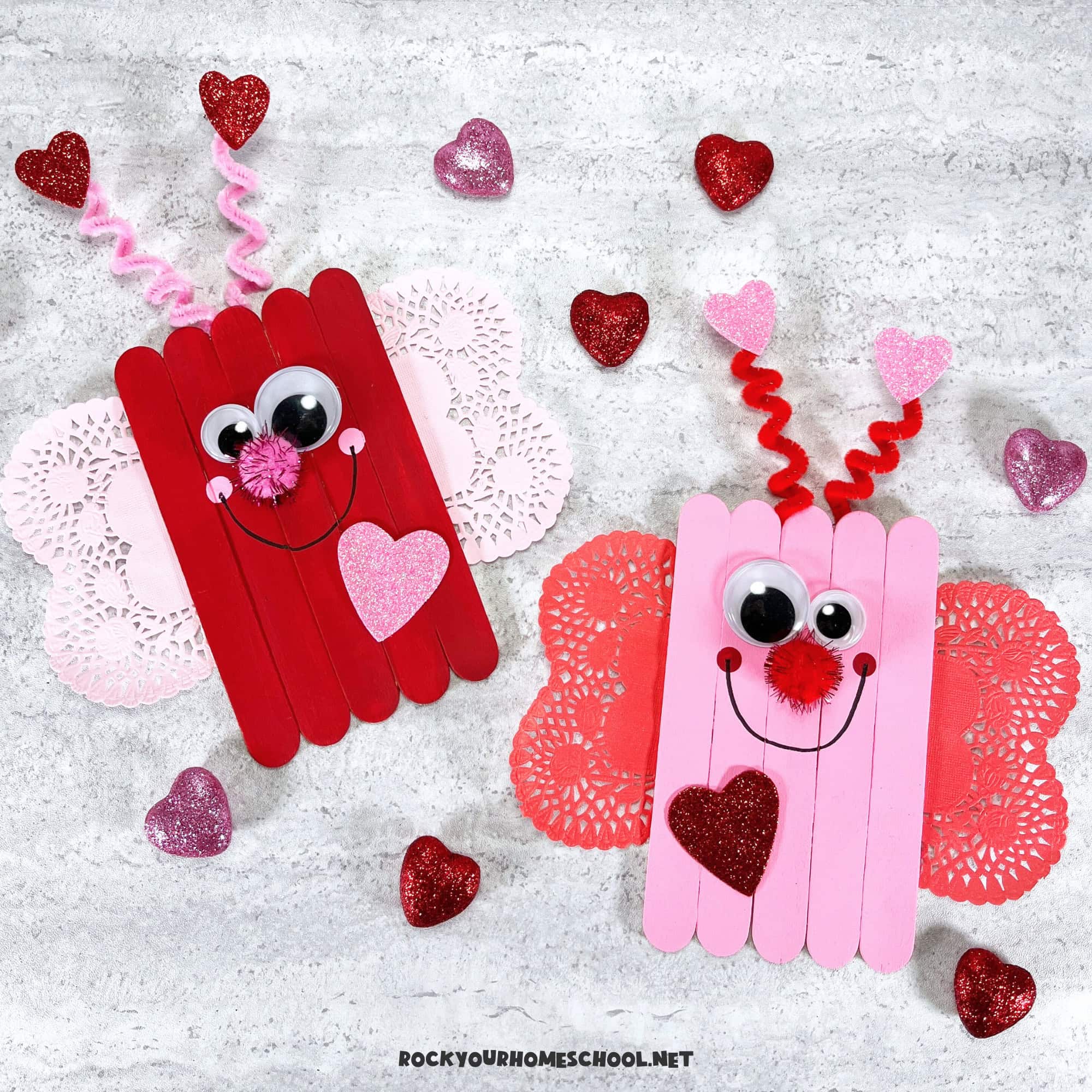 Examples of simple love bug craft for kids in red and pink made with wood craft sticks, heart-shaped doilies, and pipe cleaners.