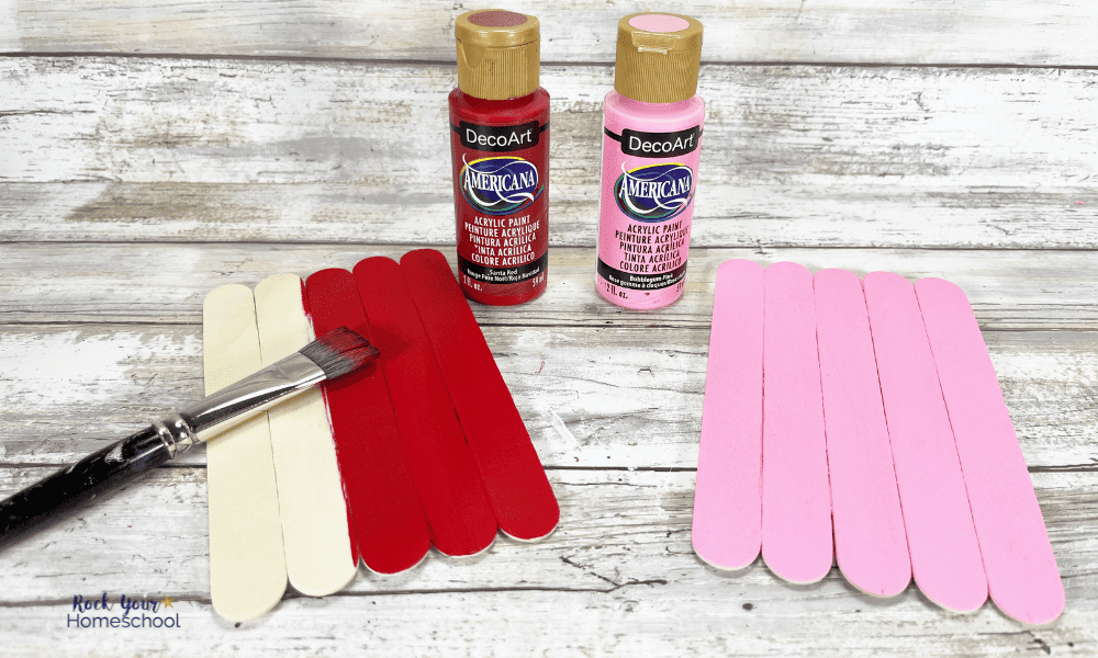 Paintbrush, jumbo craft sticks, and red and pink paint bottles for this love bug craft.