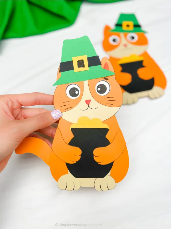 Woman holding cat leprechaun craft with example in background.