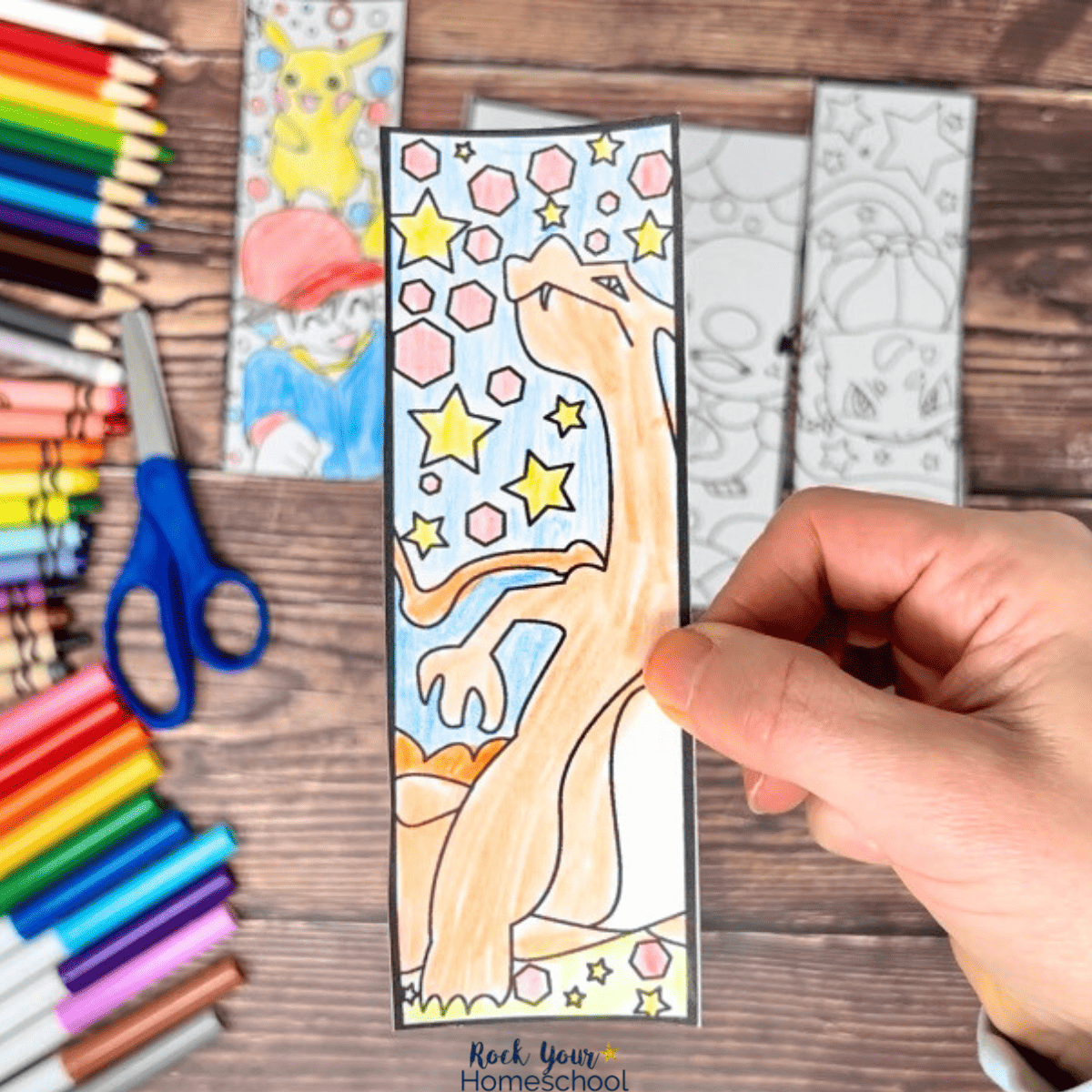 Woman holding Charizard bookmarks with other examples of free printable Pokemon bookmarks with markers, crayons, color pencils, and scissors in background.