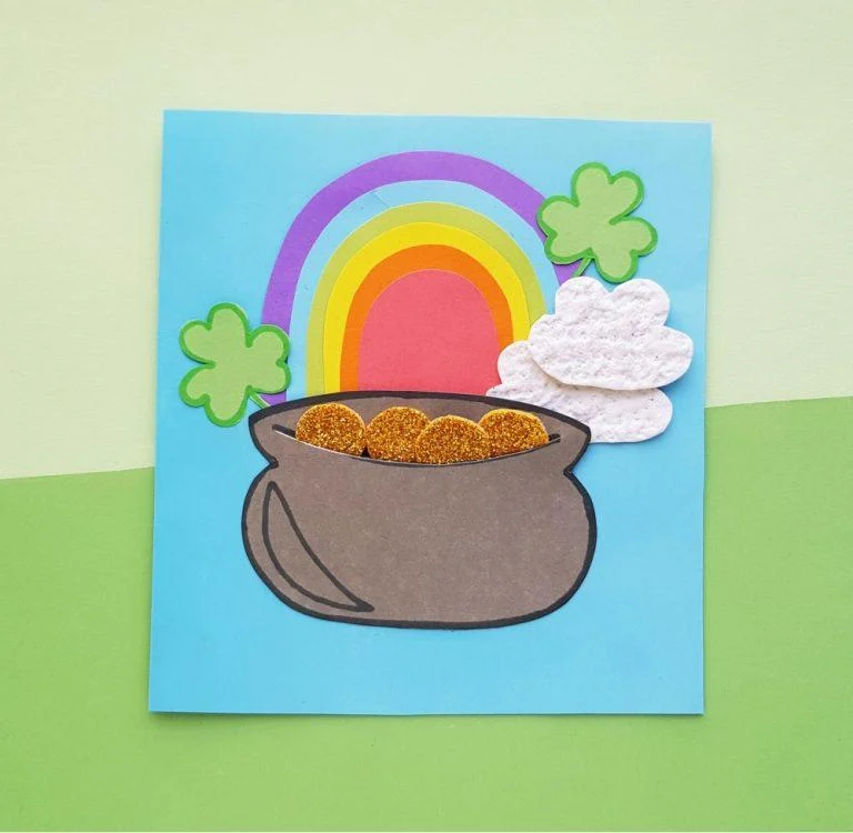 Paper craft featuring pot of gold with rainbow, clovers, and clouds.