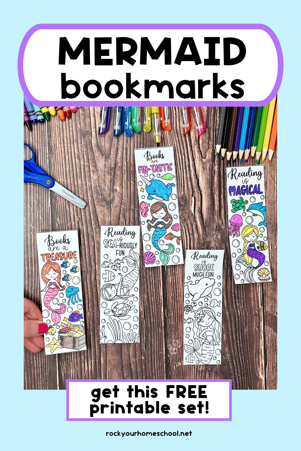 Woman holding examples of free printable mermaid bookmarks to color with glitter gel pens, color pencils, crayons, and scissors in the background.