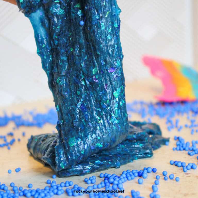 Mermaid slime in blues and greens with glitter and mermaid tail in background.