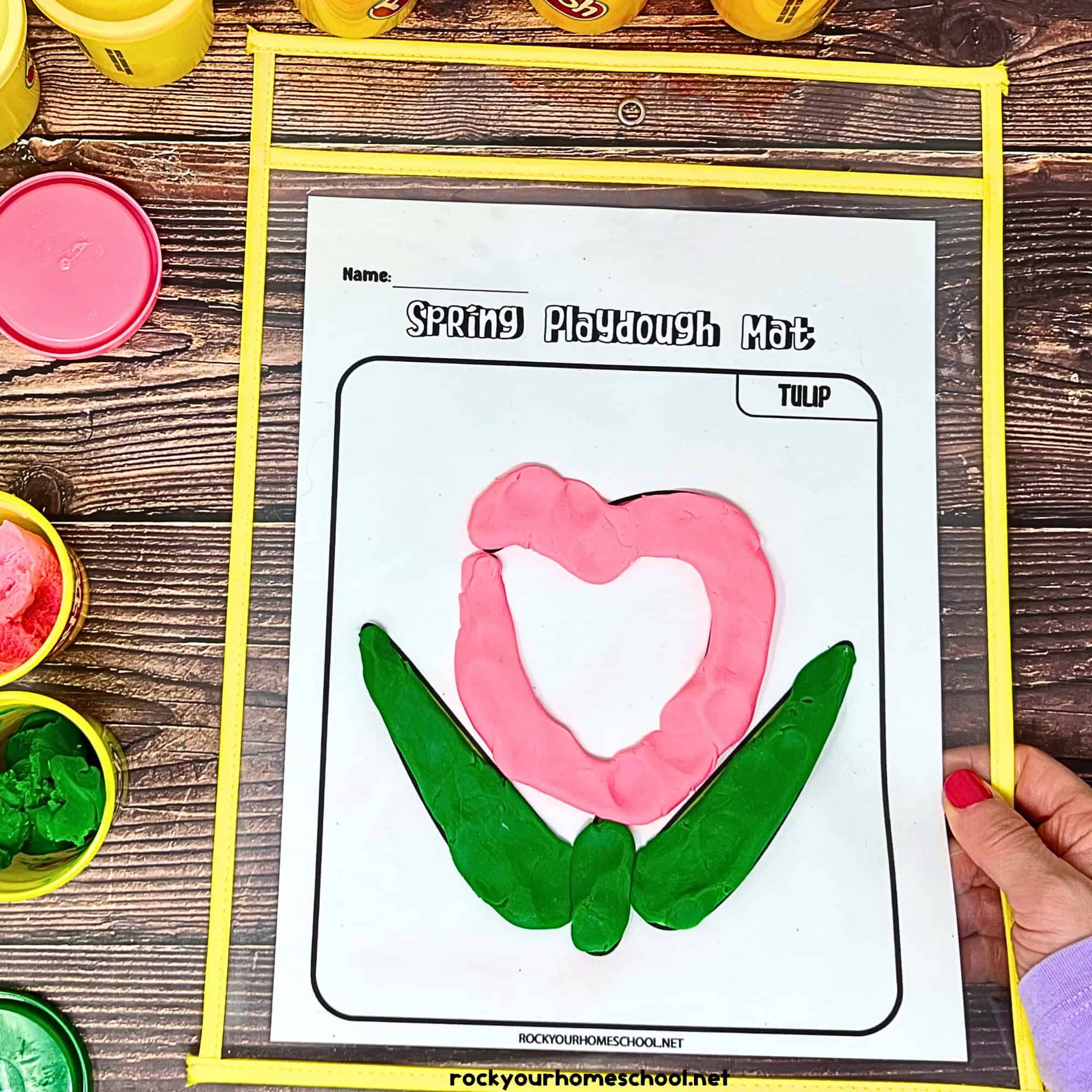 Woman holding dry erase sleeve with spring playdough mat featuring a tulip.