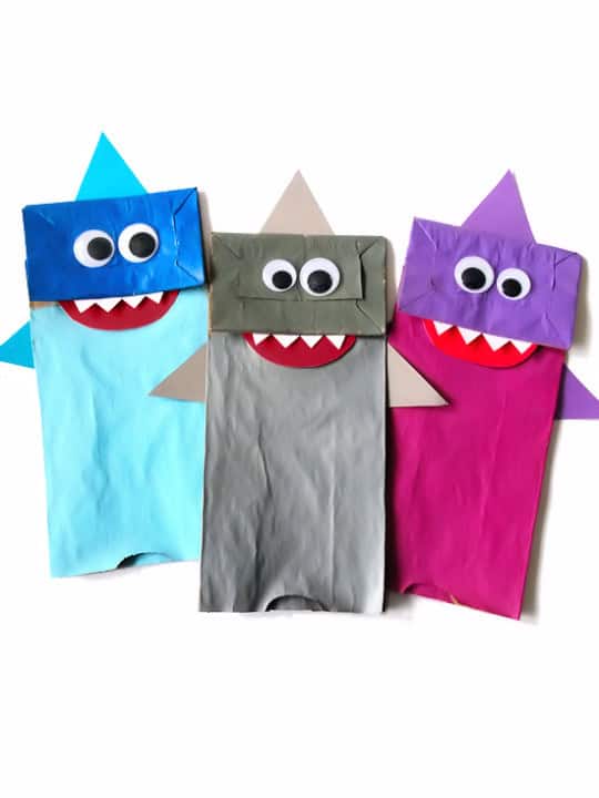 Three examples of paper bag shark crafts with googly eyes.