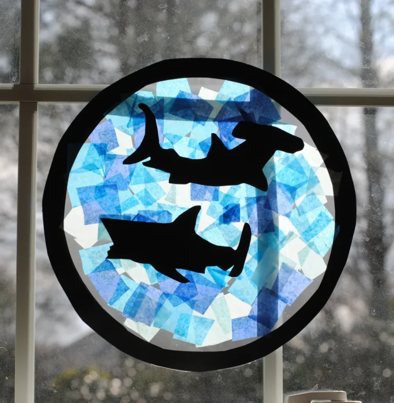 Shark porthole sun catcher craft made with construction paper and tissue paper.