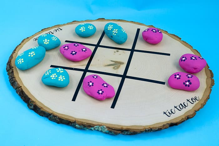Example of tic tac toe board game using slice of wood with painted rocks.