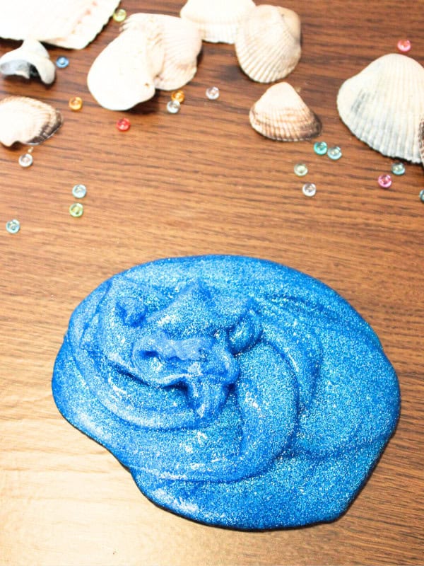 Example of DIY blue sparkly ocean slime with shells and water beads in background.
