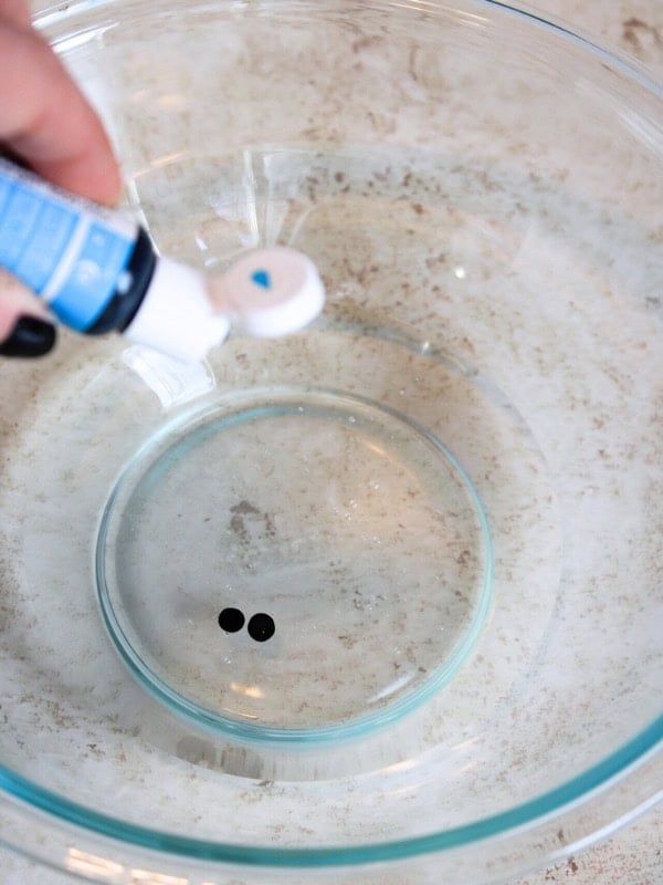 Woman adding light blue food coloring to clear glue.
