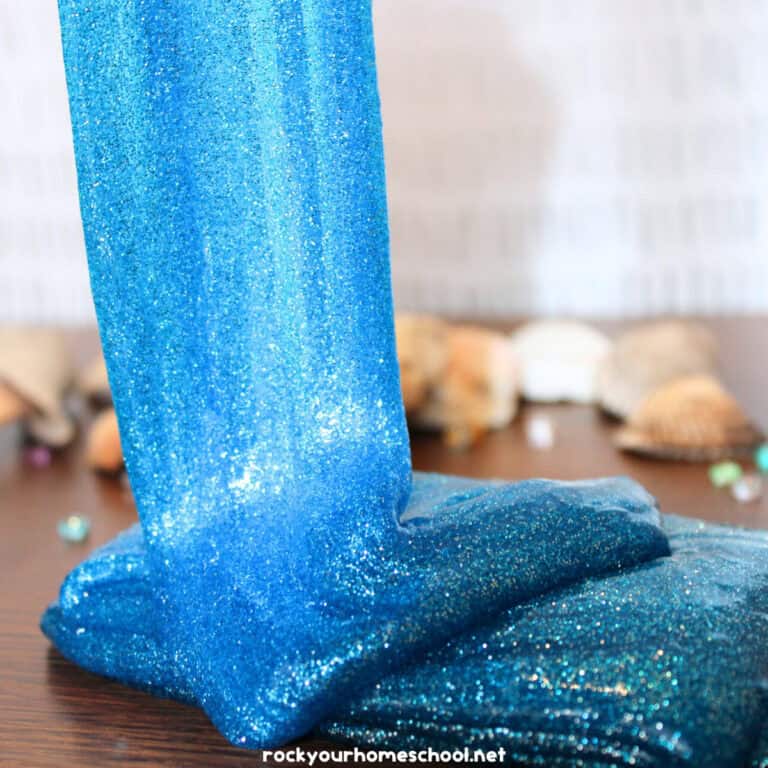 Sparkly blue ocean slime flowing onto table with shells and gems in background.
