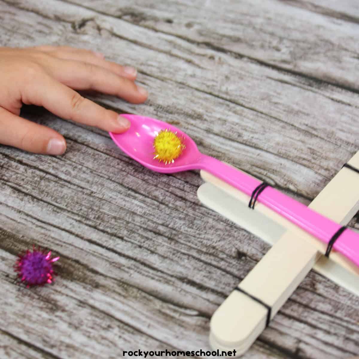 Child using STEM catapult with yellow pom pom.