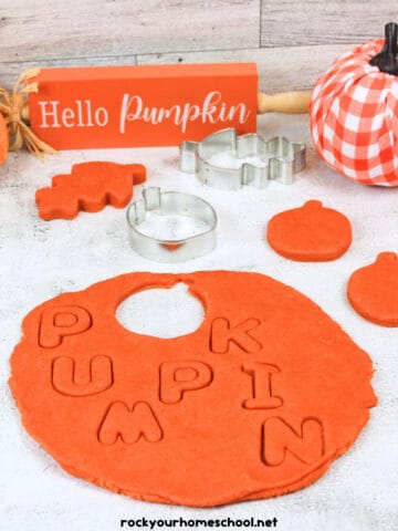 Pumpkin playdough in orange color with cookie cutters, faux pumpkins, and Hello Pumpkin sign.