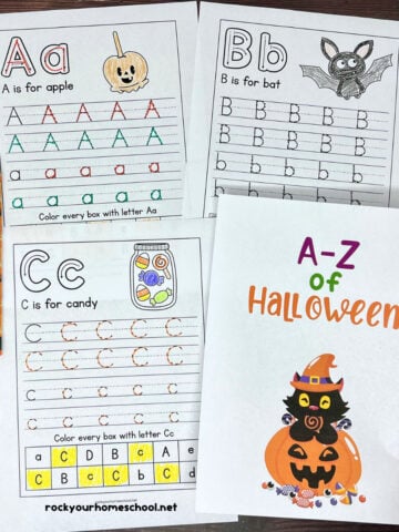 Woman holding A-Z of Halloween handwriting worksheets with examples of Aa, Bb, and Cc.